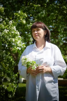 Girl walking, Relaxing near Blossoming apple Tree on Sunny Day. Portrait of Middle aged woman enjoying nature surrounded by white blossoms