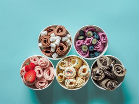 Rolled ice creams in cone cups on blue background. Different iced rolls, top view or flat lay. Thai style rolled ice cream