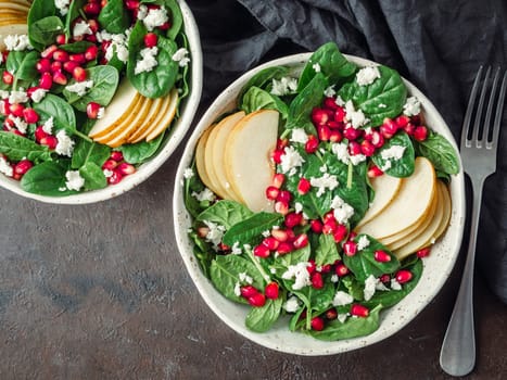 Vegan salad bowl with arugula, pear, pomegranate, cheese on black background. Vegan breakfast, vegetarian food, diet concept. Top view or flat lay. Copy space for text.