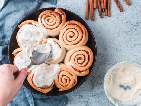 Woman's Hand Spreading Frosting on Cinnamon Rolls in Skillet. Vegan swedish cinnamon buns Kanelbullar with pumpkin spice,topping vegan cream cheese. Top view or flat lay. Copy space for text