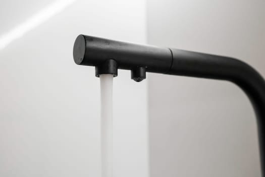 Modern black kitchen faucet with flowing tap water.