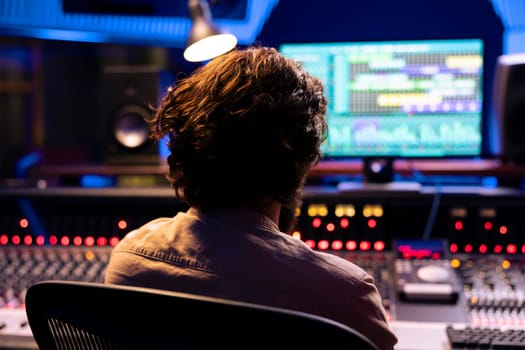 Sound designer tuning audio recordings with faders and buttons on control desk in professional music studio, mixing and mastering tracks for a new album. Adjusting volume levels with equalizer.