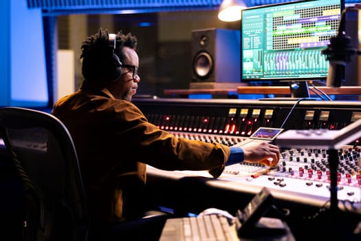 African american sound producer uses compressor and mixer in professional recording studio, adjusting volume levels and audio settings on a track. Music production concept in control room.