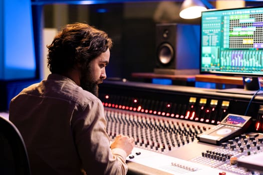 Music producer working on mixing and mastering music with daw software, editing tracks with audio console dashboard. Young sound designer creating sounds and tunes in professional studio.