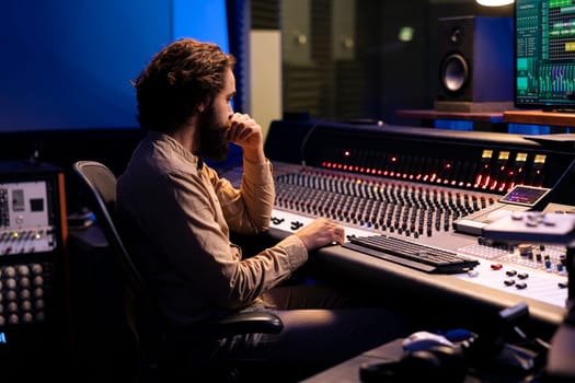 Sound designer mixing and mastering music in recording studio, examines audio digital software on pc before adding effects in post production. Technician works in control room. Close up.