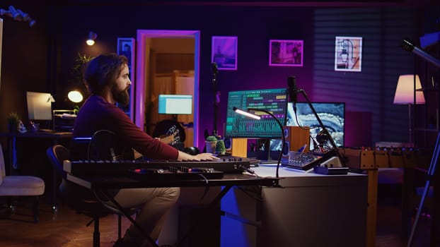 Music producer operating with electronic setup of home studio, recording acoustic guitar sounds. Artist navigating signal processing activity, utilizing digital audio workstation at desk. Camera B.