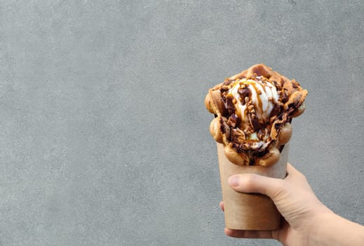 Hong Kong waffles in female hand on brick wall background. Delicious bubble waffle with ice cream and caramel syrup in woman hand. Trendy food. Copy space for text
