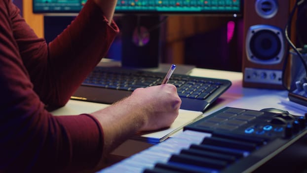 Composer developing an original track In his home studio, writing down lyrics and harmonic notes before recording the song melody. Musician using DAW computer apps for creating music. Camera A.