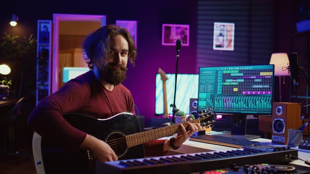 Musician plays acoustic guitar and records melody to compose new song and tunes. Computer screen showing DAW software interface with soundtracks, sound engineer in music production. Camera B.