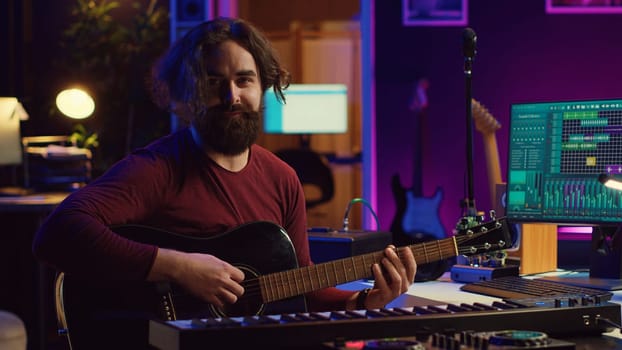 Portrait of artist recording tunes on daw software with his guitar, enjoying time in his home studio office. Audio engineer and musician creating new tracks, stereo electronic instruments. Camera A.