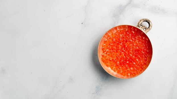 Red caviar top view or flat lay. Bowl of red caviar on white marble background. Copy space for text. Banner