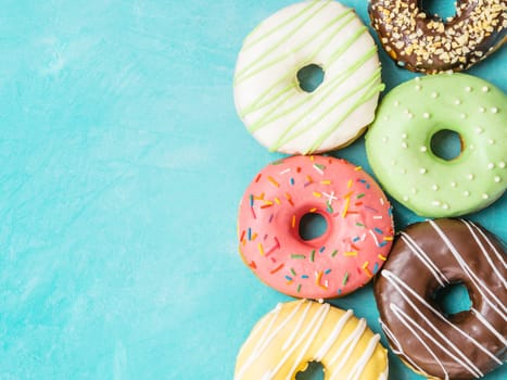 Top view of assorted donuts on blue concrete background with copy space. Colorful donuts background. Various glazed doughnuts with sprinkles.