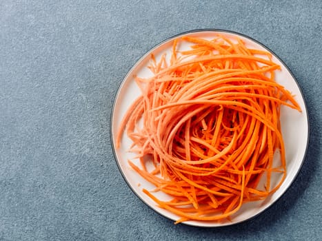 Carrot noodles on plate overhead.Vegetable noodles - orange sweet carrot spaghetti on plate over gray stone background.Clean eating,raw vegetarian food concept.Flat lay or top view.Copy space for text