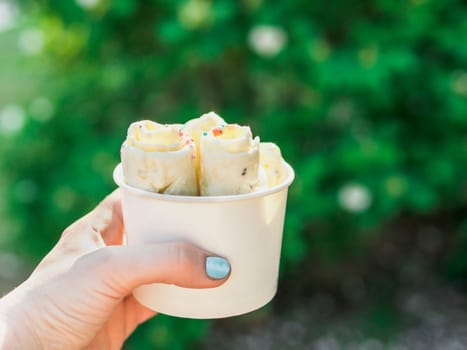 Rolled ice cream in cone cup in woman hand. Woman holds cone cup with thai style kiwi banana rolled ice cream. Outdoor. Natural daylight Copy space for text or design.