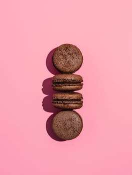 Chocolate macarons with copy space. Row of perfect french macarons or macaroons on pink background. Top view or flat lay. Hard light