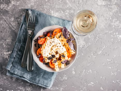 Tasty italian fusilli pasta with cherry, mozarella or buratta cheese and fresh basil. Dish with pasta on gray concrete background. Top view. Copy space. Healthy food concept and recipe idea.