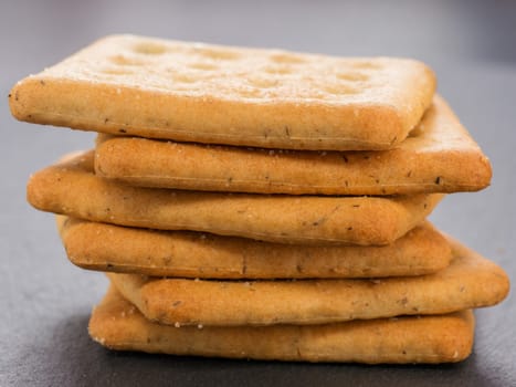 stack of square crackers on slate gray background. Dry salt cracker cookies with fiber and dry spices