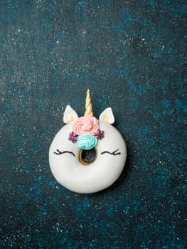 Unicorn donut over dark background. Trendy donut unicorn with white glaze. Top view or flat lay. Copy space for text. Vertical.