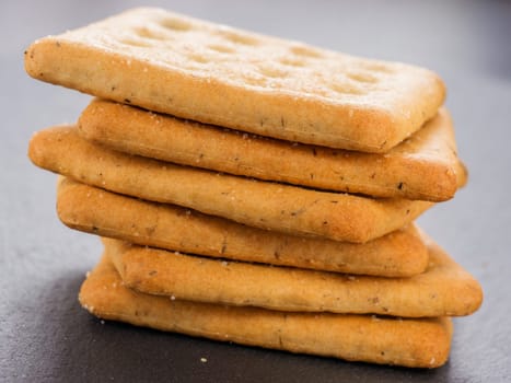 stack of square crackers on slate gray background. Dry salt cracker cookies with fiber and dry spices