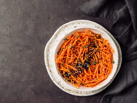 Spicy sesame carrot noodles salad ready-to-eat overhead. Vegetable carrot spaghetti with black sesame and thyme. Clean eating, raw vegetarian food concept. Flat lay or top view. Copy space for text.