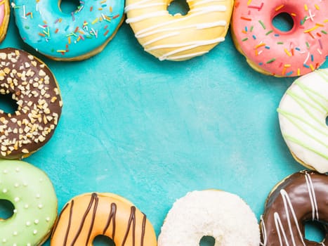 Top view of assorted donuts on blue concrete background with copy space. Colorful donuts background. Various glazed doughnuts with sprinkles.