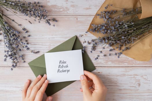 RELAX REFRESH RECHARGE text on supportive message paper note reminder from green envelope. Flat lay composition dry lavender flowers. Concept of inner happiness, slowing-down digital detox personal fulfillment. Top view