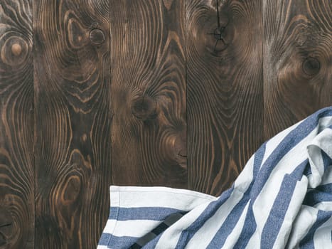 View from above on brown wooden table with linen kitchen towel or textile napkin. Blue tablecloth on dark brown wood tabletop. Copy space for text. Can use as mock up for design