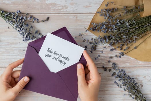 TAKE TIME TO MAKE YOUR SOUL HAPPY text on supportive message paper note reminder from green envelope. Flat lay composition dry lavender flowers. Concept of inner happiness, slowing-down digital detox personal fulfillment. Top view