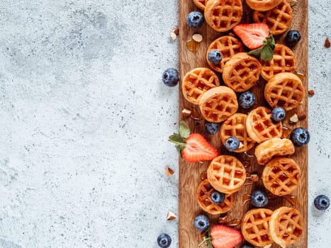 Small round delicious soft belgian waffles on cutting board. Fresh belgian waffles with berries and caramel sauce top view. Copy space for text or mock up