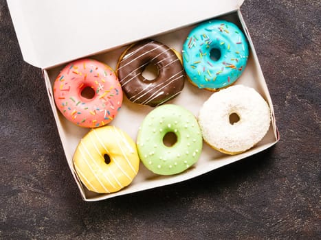 Top view of paper box with colorful donuts on dark cement background. Copy space.