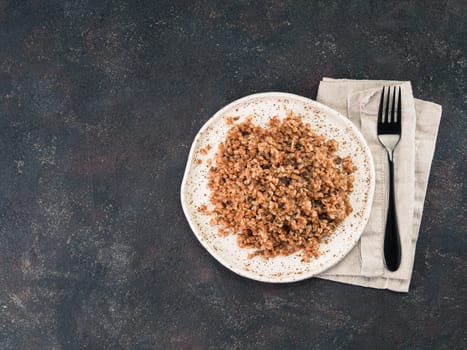Buckwheat risotto with dried mushrooms in craft plate on black cement background. Gluten-free and vegetarian buckwheat recipe ideas. Copy space. Top view or flat-lay.