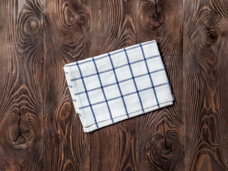 View from above on brown wooden table with linen kitchen towel or textile napkin. Blue tablecloth on dark brown wood tabletop. Copy space for text. Can use as mock up for design