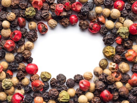 Mixed peppercorns background with white copy space in center. Food background with peppercorns. Different colored peppercorns pattern on white background, top view or flat lay