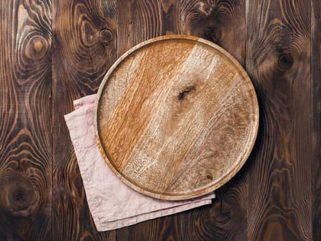 Empty wooden plate and textile napkin over brown wooden table. Top view or flat lay. Mock up for design, menu, food delivery. Copy space for text