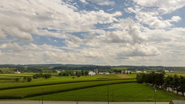 The vastness of the farmland stretches out beneath a sky dotted with fluffy clouds, encapsulating the open space and serenity of rural life.