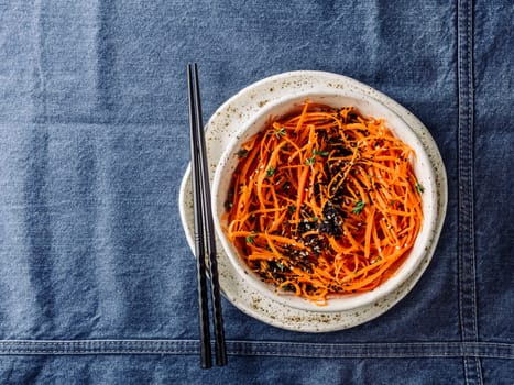 Spicy sesame carrot noodles salad ready-to-eat overhead. Vegetable carrot spaghetti with black sesame and thyme. Clean eating, raw vegetarian food concept. Flat lay or top view. Copy space for text.