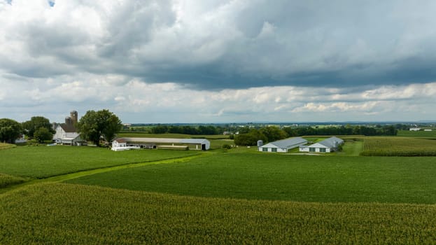 A peaceful farming homestead lies under a dramatic sky, where the dense clouds hint at the changing weather over the lush landscape.