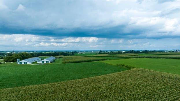 Dark, brooding clouds loom over a tranquil expanse of farmlands, offering a dramatic contrast to the peaceful greens below.