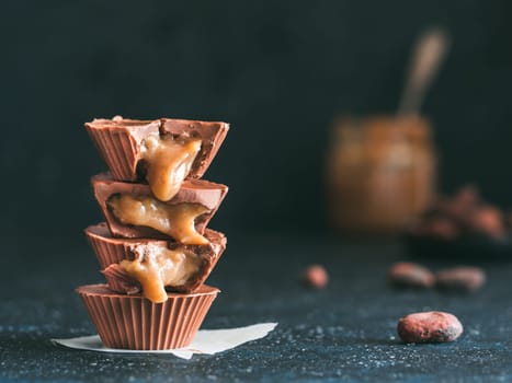 Stack of vegan chocolate cups with caramel on dark tabletop. Homemade vegetarian chocolate caramel cups with raw cacao chocolate. Ideas and recipes for healthy sweets and dessert. Copy space for text