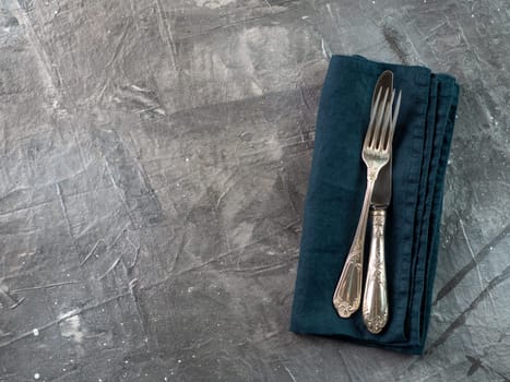 Silver fork and knife on dark green emerald linen napkin over gray textured background table with copy space. Cutlery with copy space, top view or flat lay