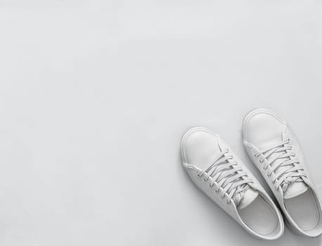 White leather sneakers on white background. Pair of fashion trendy white sport shoes or sneakers with copy space for text or design. Overhead shot of new white sneakers,monochrome.Top view or flat lay