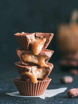 Stack of vegan chocolate cups with caramel on dark table. Homemade vegetarian chocolate caramel cups with raw cacao chocolate. Ideas and recipes for healthy sweet dessert. Copy space for text.Vertical