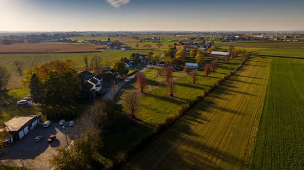 Aerial view of a sprawling farmland at sunset with long shadows, showcasing autumn's touch on trees and fields, perfect for themes of harvest, rural planning, and seasonal changes.