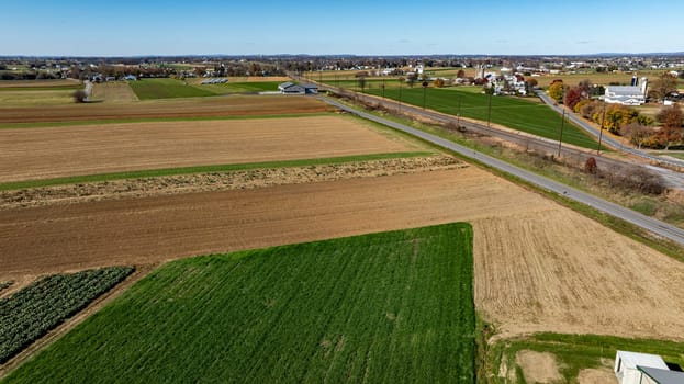 An expansive drone capture of farmland alongside a country road, showcasing a mix of fallow and verdant plots, suitable for discussions on rural development and land use.