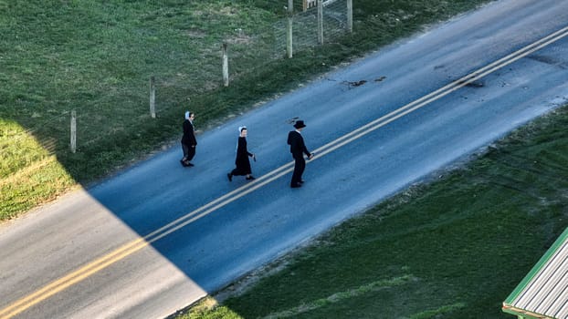 Ronks, Pennsylvania November 14, 2023 - Captured from above, three Amish people enjoy an evening promenade, their figures etched against the road by the waning light.