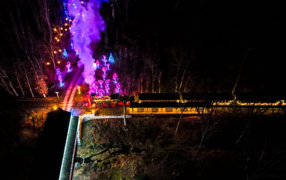 Aerial View Of A Vibrantly Lit Train Emitting Purple Smoke As It Passes Through A Forested Area At Night.