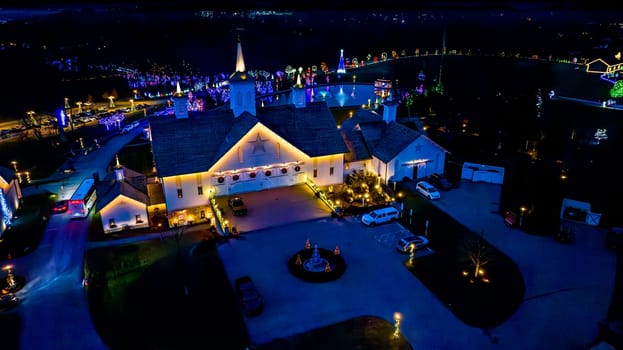 Overhead Night View Of A Complex With Buildings Outlined In Lights, A Central Pond, And A Surrounding Drive Lined With Lit Trees.