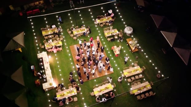 Aerial view of a lively outdoor gathering at night with guests and string lights