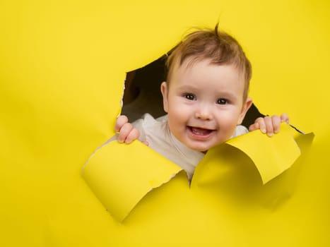 Cute Caucasian baby sticking out of a hole in a paper yellow background