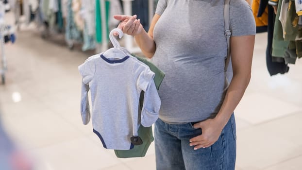 Caucasian pregnant woman chooses baby clothes in a store. Faceless expectant mother in the 3rd trimester